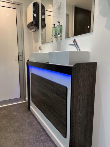 Modern restroom with two sinks, backlit vanity, soap dispensers, and a mirror.