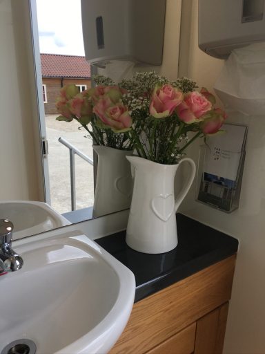 A white pitcher filled with pink flowers on a black countertop near a sink.