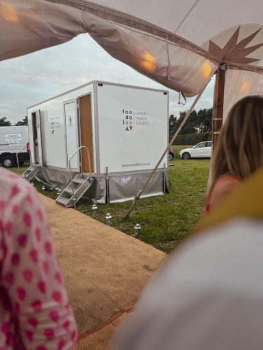 A white portable unit in a grassy area, partially obscured by people in the foreground.