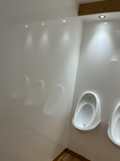 Modern restroom with three white urinals and soft overhead lighting.