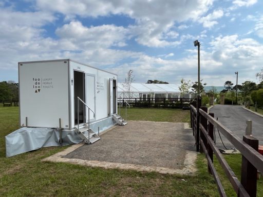 A portable building on a grassy area with a cloudy sky and trees in the background.