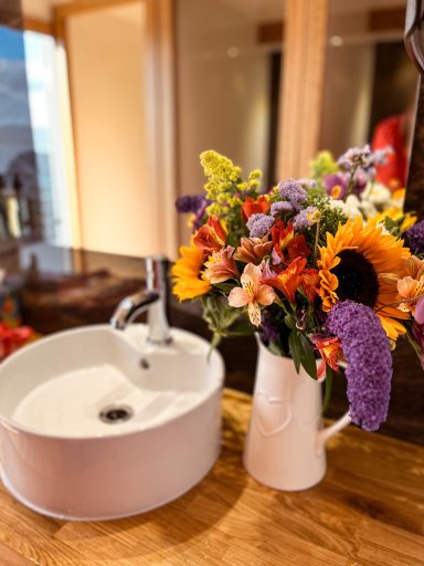 A white sink beside a vibrant bouquet of sunflowers and mixed flowers on a wooden surface.